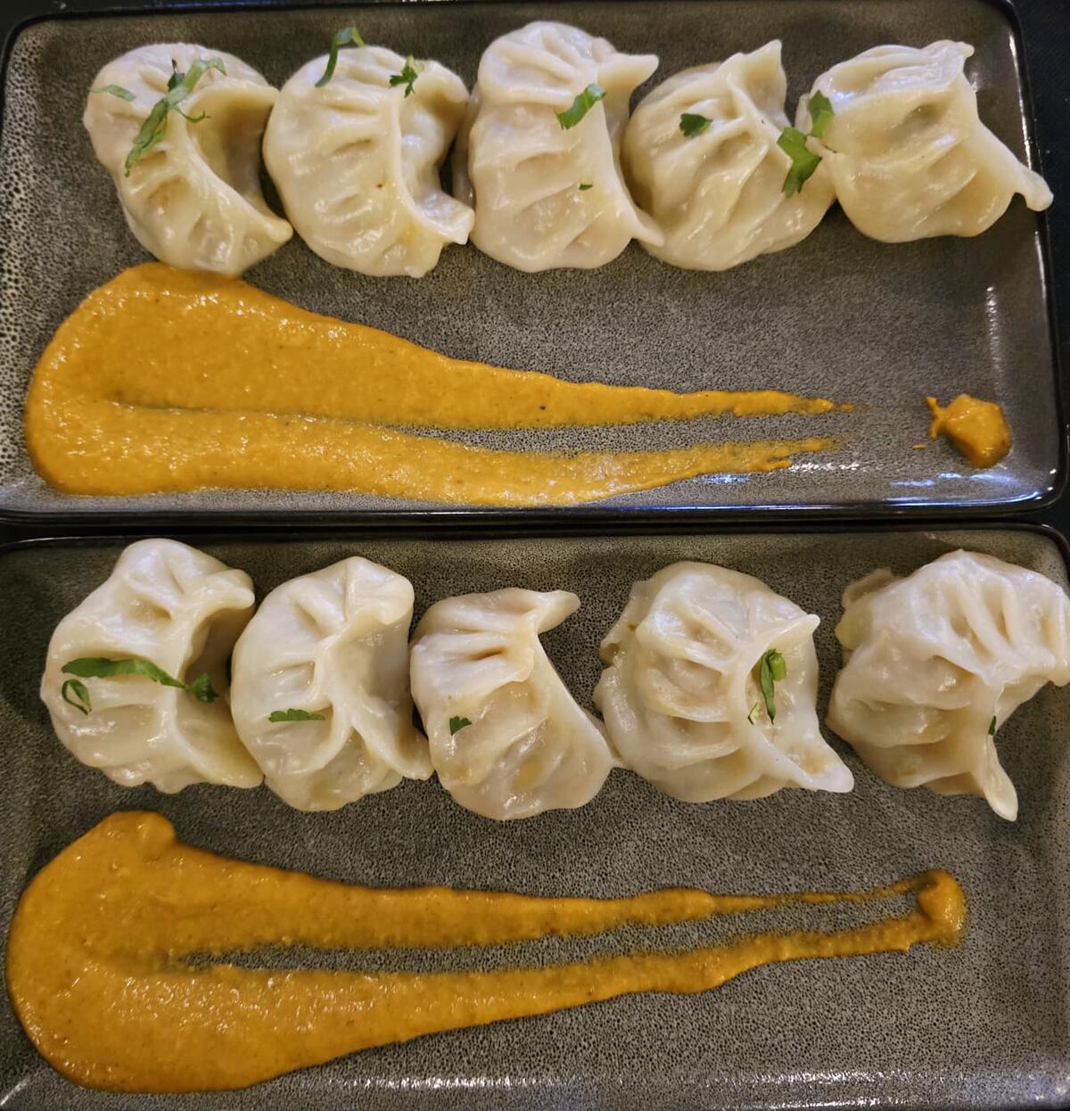 Two plates of steamed momo dumplings with a swipe of dipping sauce